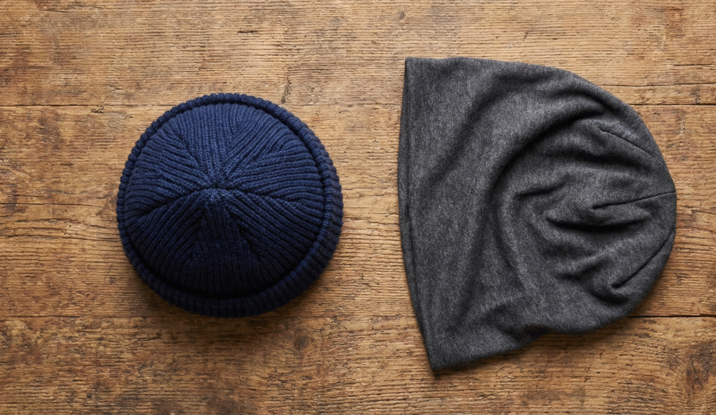 Top-down comparison of a structured navy blue watch cap with a folded cuff versus a loose grey slouchy beanie made of jersey knit.