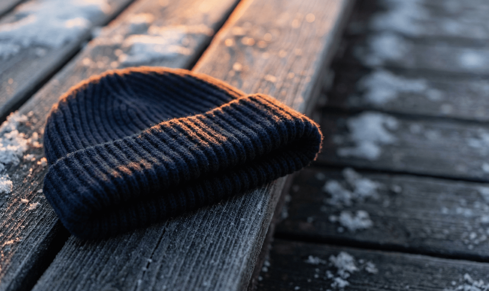Close-up of a navy blue ribbed beanie lying on frosty wooden planks, showing the thick folded cuff and warm texture.