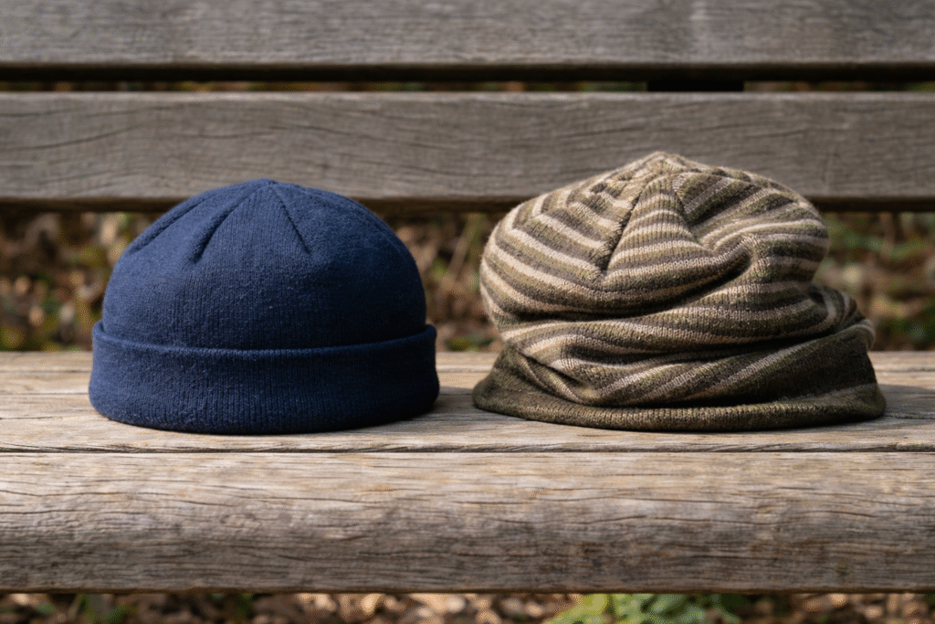 Two beanie hats on a wooden bench, one solid navy blue and one striped olive green knit