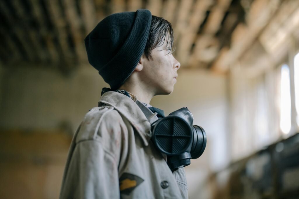Person wearing a black beanie and protective respirator mask standing inside an industrial warehouse with soft natural light