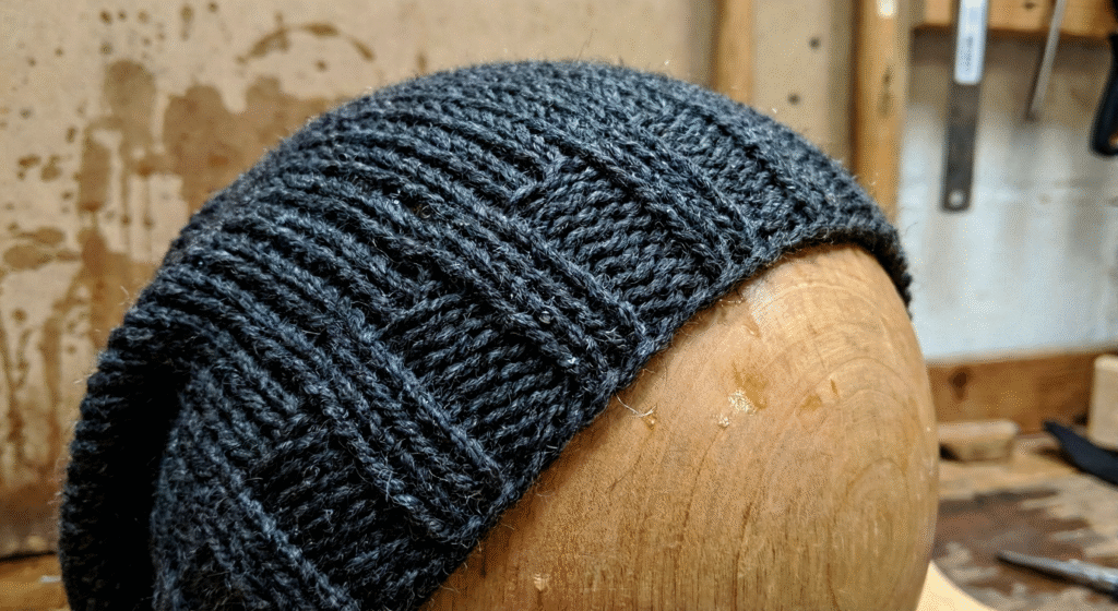 A black slouchy knit beanie displayed on a neutral mannequin head against a plain white background.